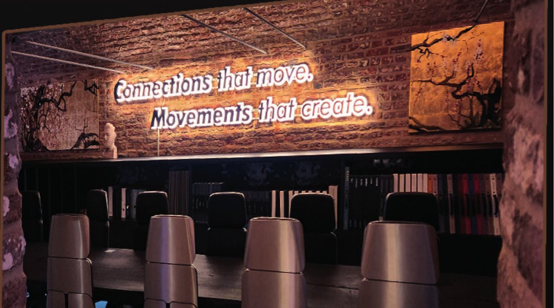 Bar mit Neonschriftzug „Connections that move. Movements that create.“ vor Ziegelwand